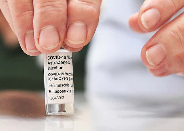 A hand holds a vial of the AstraZeneca vaccine.