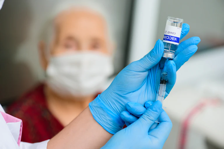 Nurse drawing up COVID vaccine into syringe for elderly person