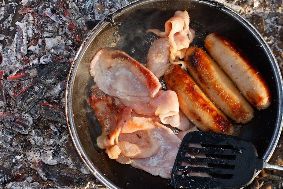A pan of bacon and sausages being cooked on an outdoor fire.