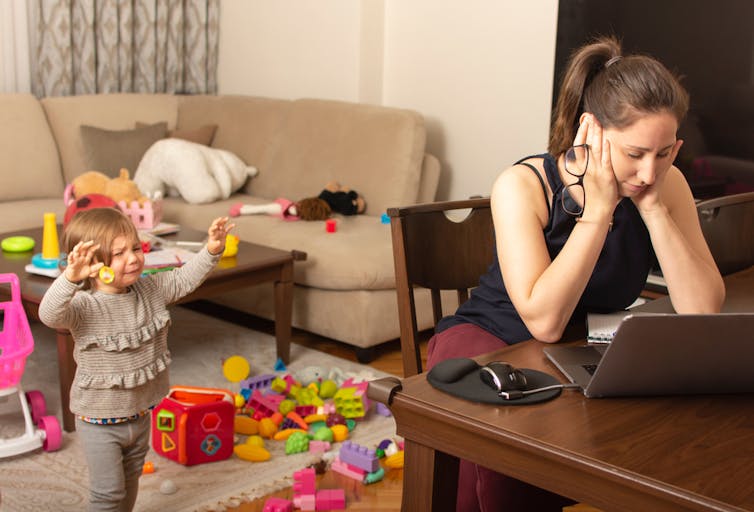 Woman looks at laptop while child cries in background