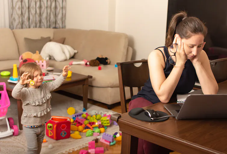 Woman looks at laptop while child cries in background