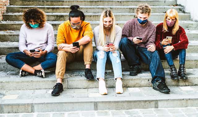 Five young people sit on steps looking at phones