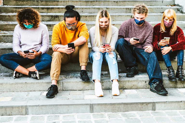 Five young people sit on steps looking at phones