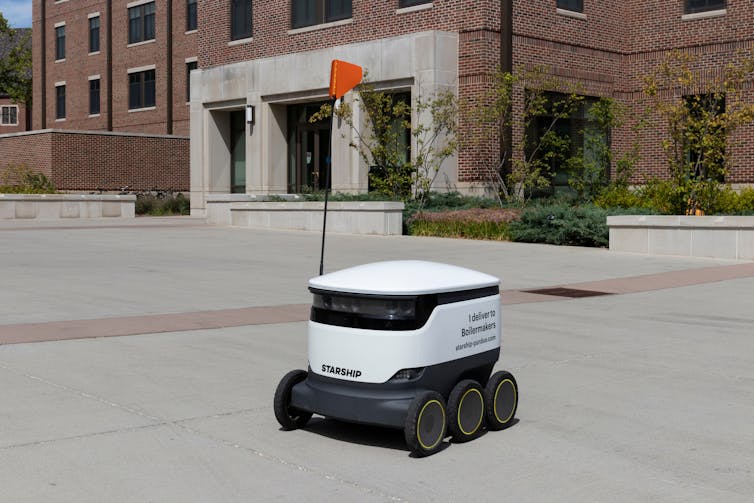 A small trolley-like robot with a flag on a city street.