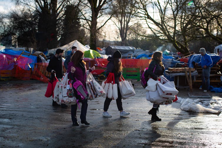 People carrying bags of donations to a homeless camp.
