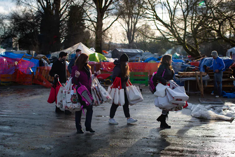People carry bags of donations to a homeless encampment.