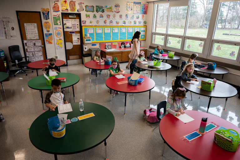A teacher walks around masked students in a classroom.