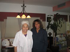 Two women, one younger and one older, stand facing the camera, smiling.