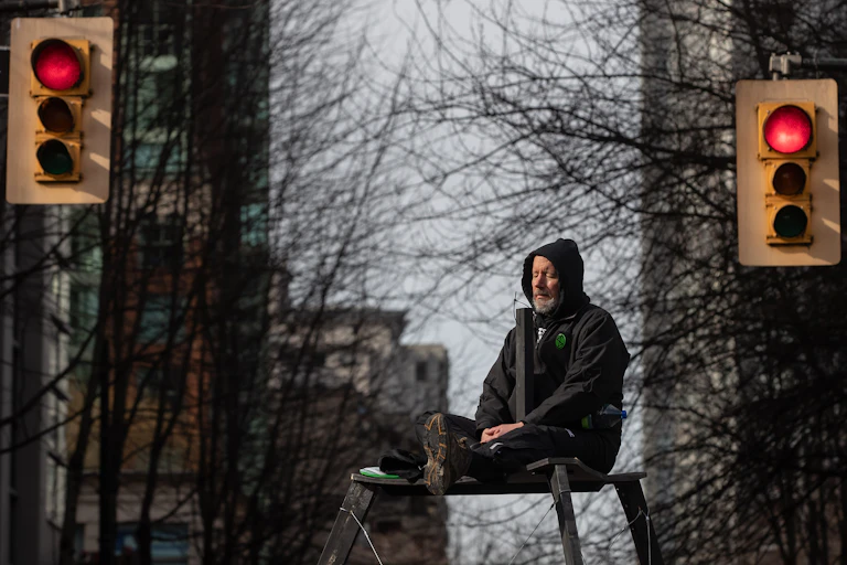 A protester sits on a tripod platform high above the street between two red lights.