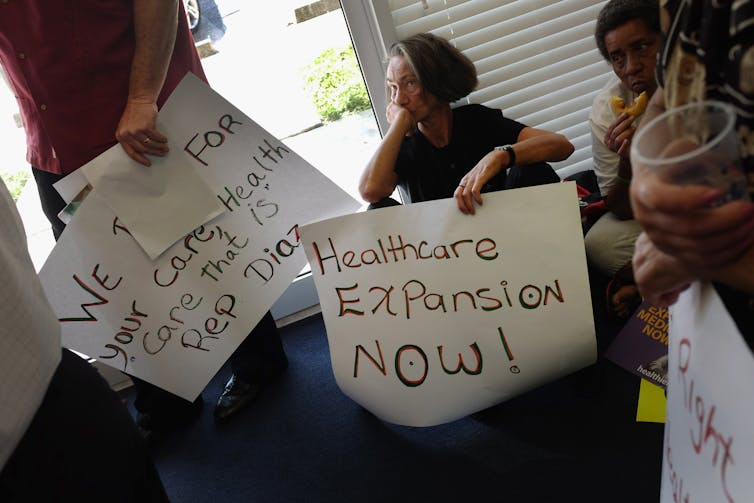 Protesters carrying signs that call for Medicaid expansion.