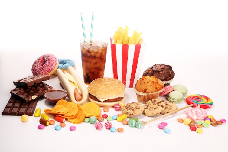 An assortment of unhealthy foods, including a hamburger, soda, crisps, chocolate, and candy.