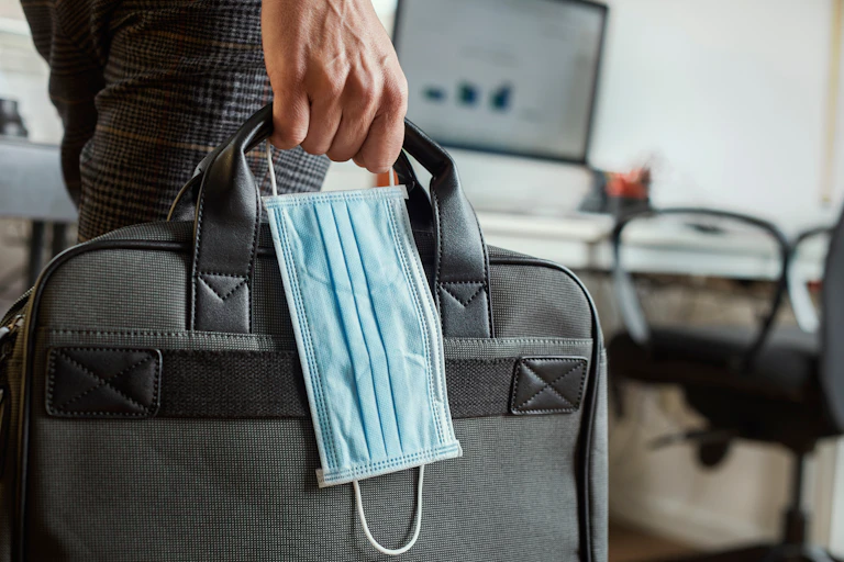Man holds briefcase and surgical mask.