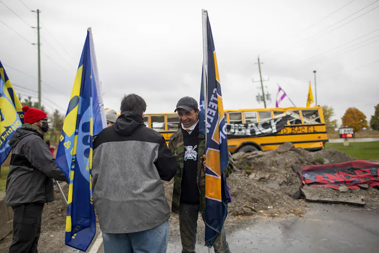 Men holding flags in front of bus that reads 'LAND BACK'