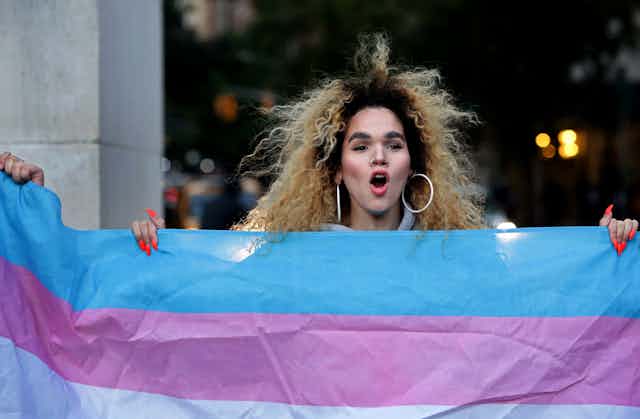 A trans woman holds a transgender pride flag