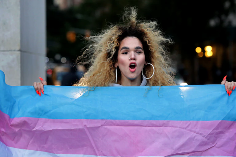 A trans woman holds a transgender pride flag