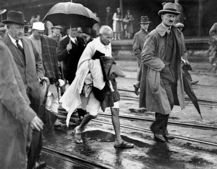 Gandhi walks in his dohti next to men in suits.