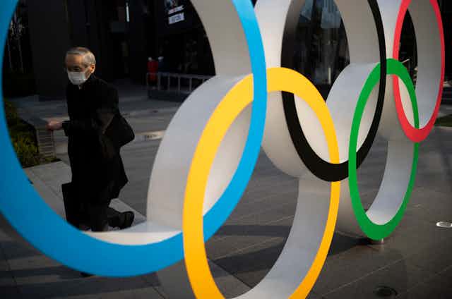 Man wearing mask walks behind Olympic rings