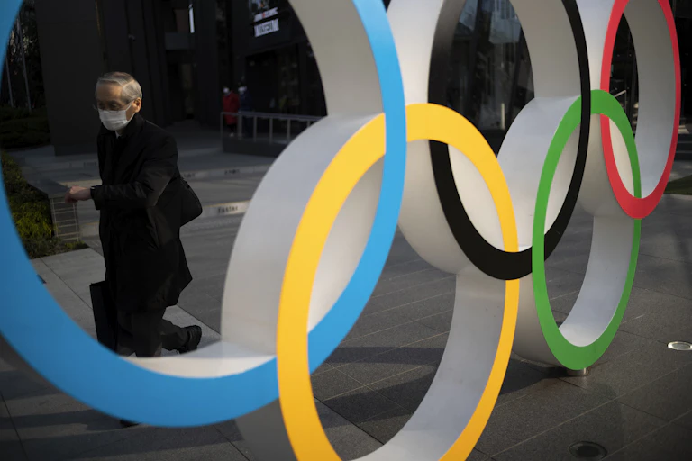 Man wearing mask walks behind Olympic rings