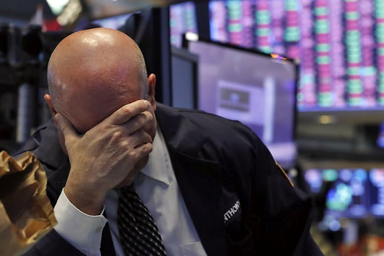 A stock trader presses his hand to his head on the floor of the New York Stock Exchange.
