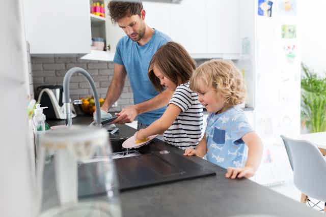 Father washing dishes with children.