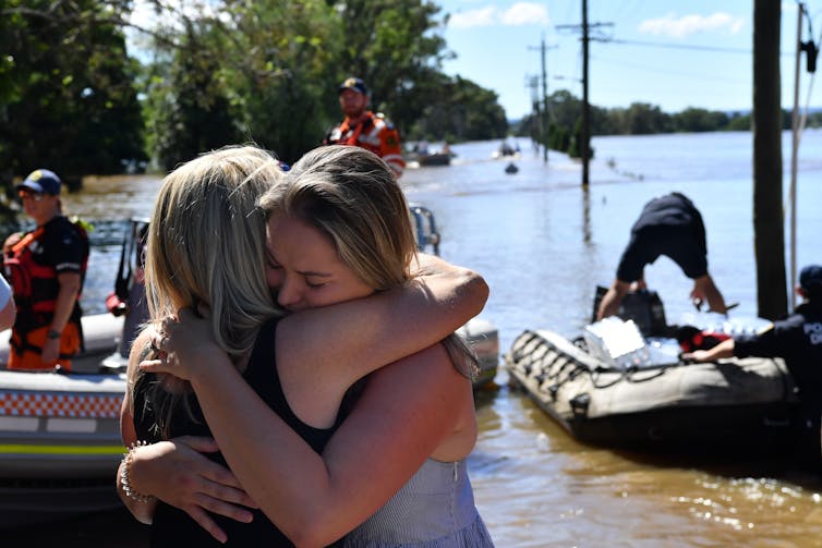 Mother and daughter hugging in foreground of floodwaters