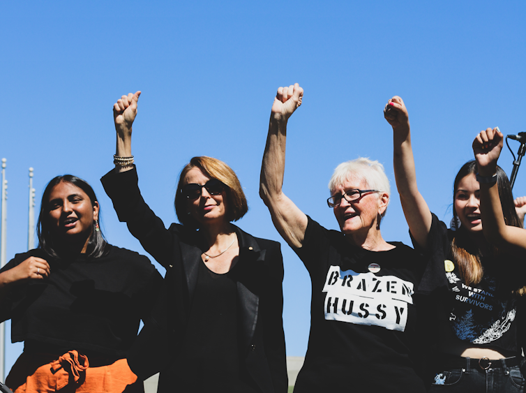 Four women of different ages stand with a fist in the air.