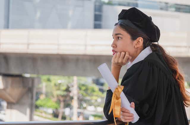 Young female graduate holding degree certificate and looking pensive