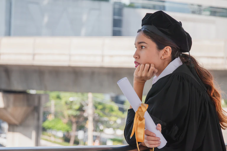 Young female graduate holding degree certificate and looking pensive