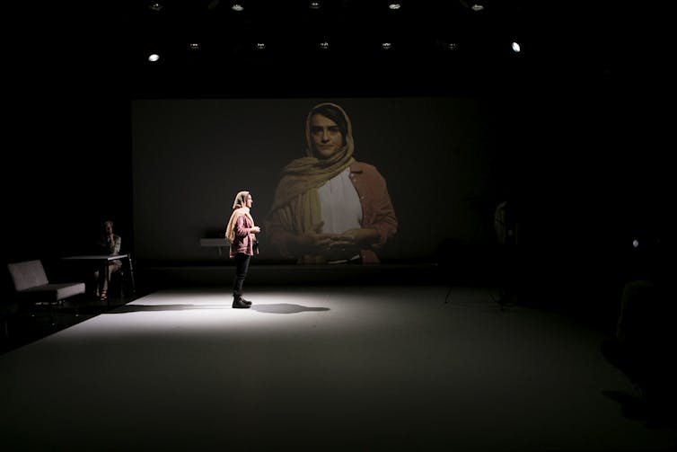 A woman on stage with a scarf loose around her head.