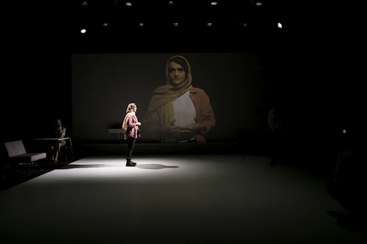 A woman on stage with a scarf loose around her head.