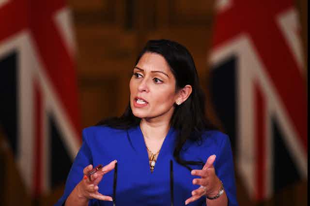 Priti Patel giving a speech in front of two Union Jack flags