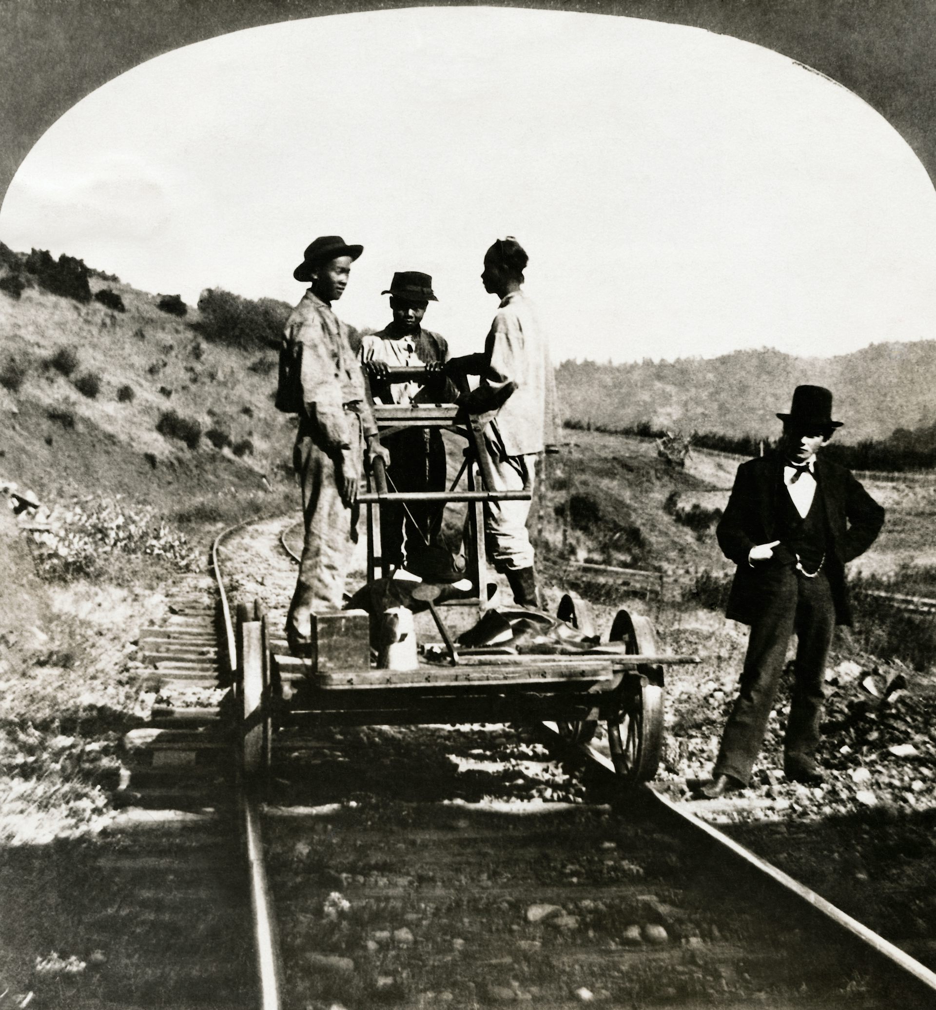 Three Asian-American men stand on a railroad pushcart