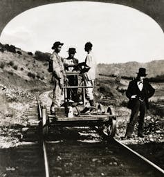 Three Asian-American men stand on a railroad pushcart