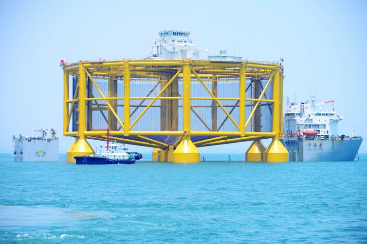 Boats move a 100-foot-tall circular pen through ocean waters.