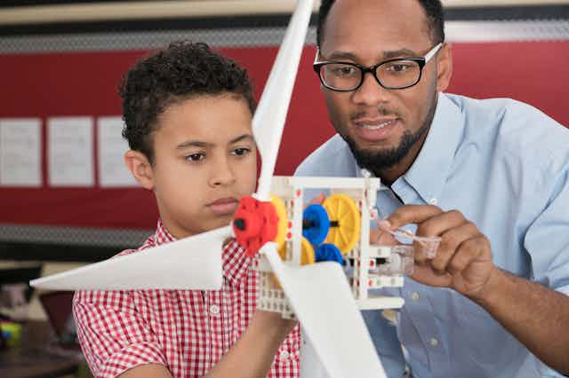 An African American students and his science teacher use a model wind turbine together in class.