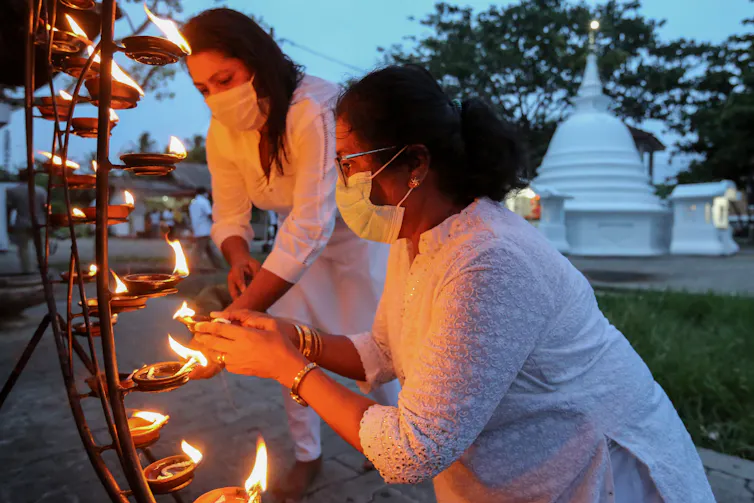 Two women dressed in white and wearing face masks light candles at a Buddhist shrine in Colombo, Sri Lanka.