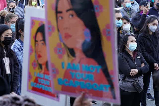 A poster that says "I am not your Scapegoat" is held up at a protest. 