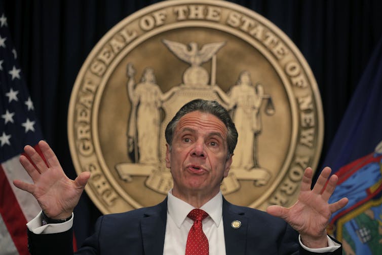 New York Gov. Andrew Cuomo gestures with his hands during a news conference with the seal of New York behind him
