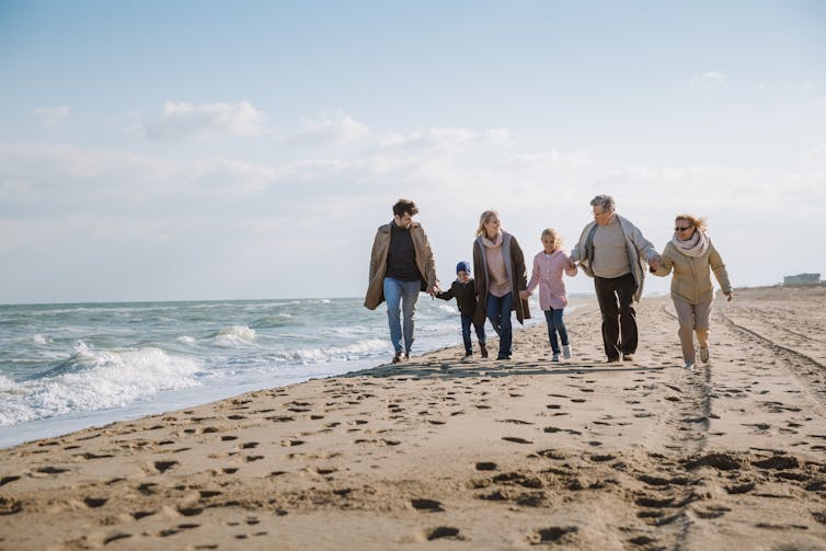 Multigenerational family, walking, holding hands on the beach.