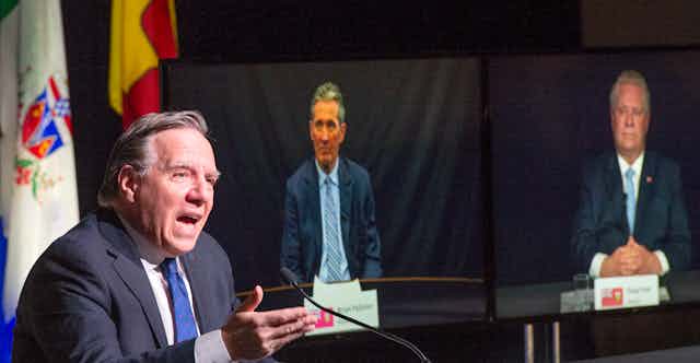 QuébecFrancois Legault speaks as Brian Pallister and Doug Ford appear on video screens behind him.