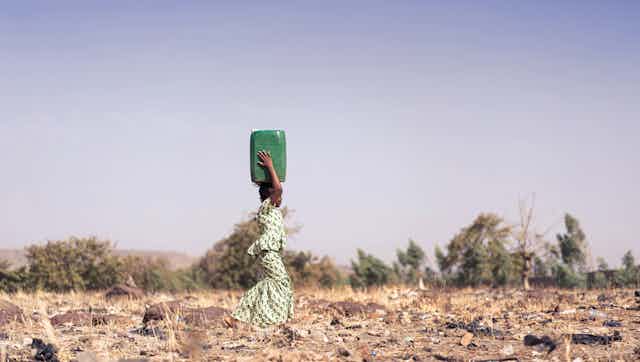 A girl carries water through dry landscape