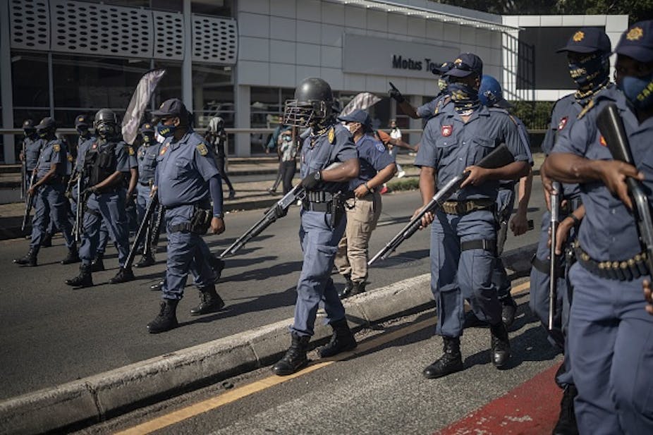 Police carrying shotguns that fire rubber bullets walk towards protesting students