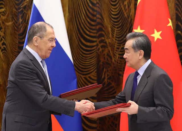 Russian Foreign Minister Sergei Lavrov (L) and Chinese Foreign Minister Wang Yi (R) exchanging documents in front of the Russian and Chinese flags.