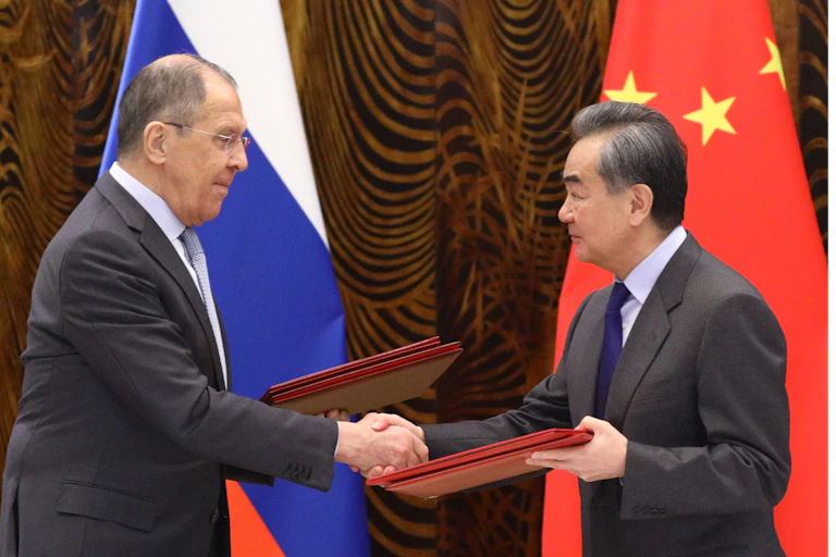 Russian Foreign Minister Sergei Lavrov (L) and Chinese Foreign Minister Wang Yi (R) exchanging documents in front of the Russian and Chinese flags.