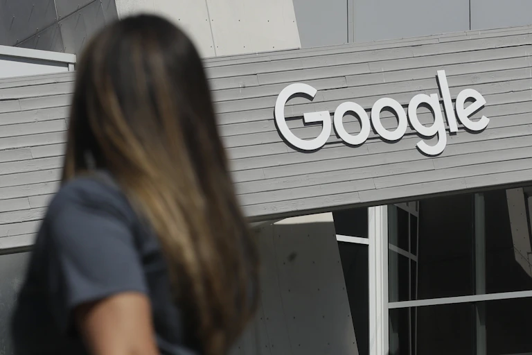 A woman is seen from behind as she walks past a building with a large Google sign.