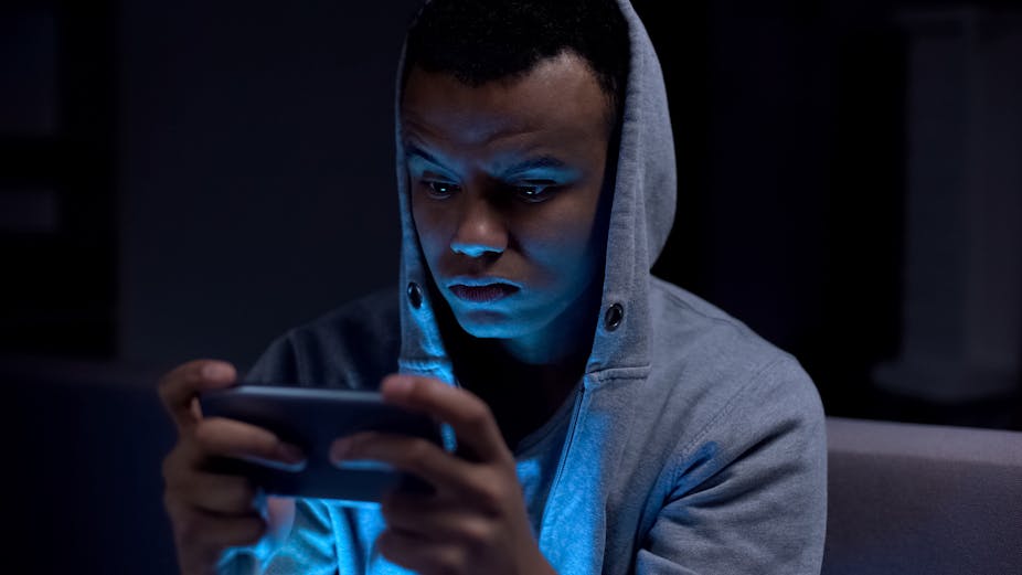 Teenage boy in grey hoodie looking at phone in the dark