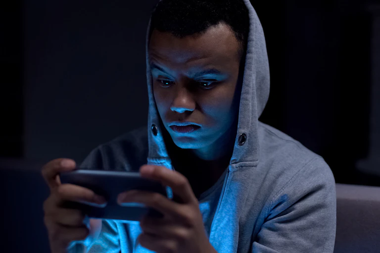 Teenage boy in grey hoodie looking at phone in the dark