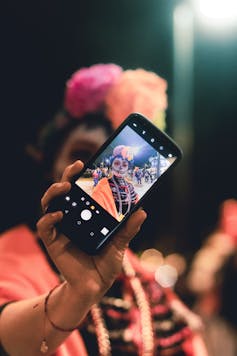 A woman in costume holds up a smartphone with a selfie she's just taken