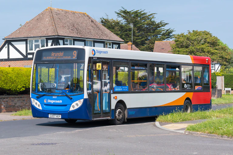 A bus drives through a leafy residential area on a summer's day.
