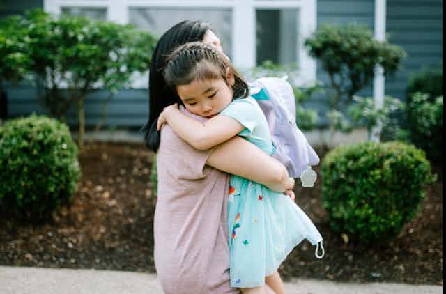 An Asian American mother hugs her daughter on a sidewalk.